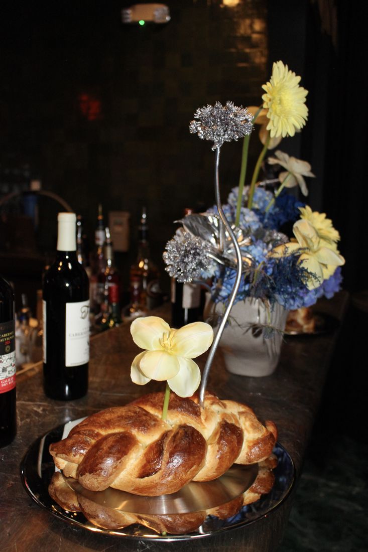 A braided challah under yellow and blue flowers at a Challah Baby Shabbat dinner